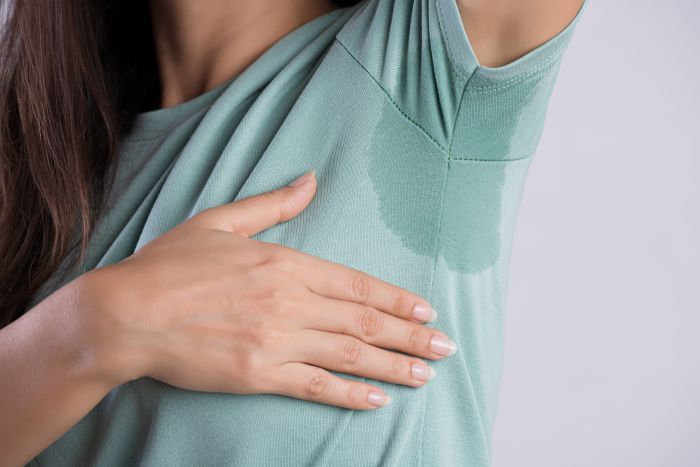 Woman with a sweat stain under the armpits of her green shirt.